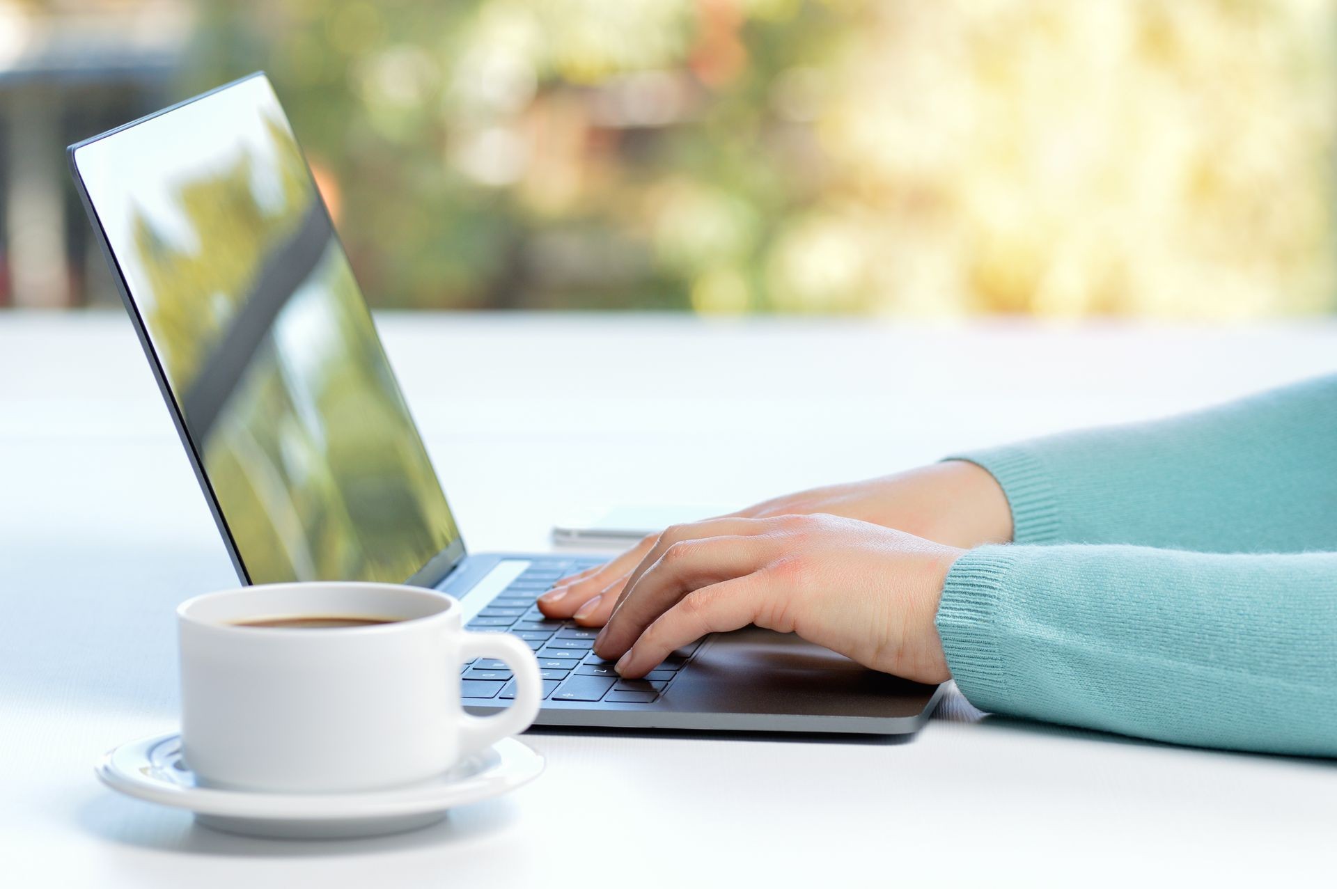 Close up of a woman hands typing in a laptop in a coffee shop terrace in the street with lens flare